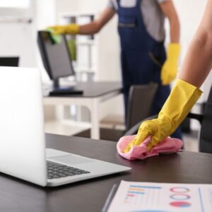 Professional office cleaner wiping a desk with yellow gloves at The Spotless Crew